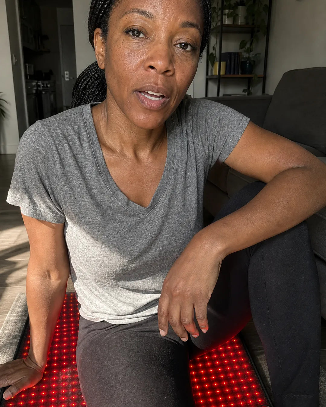 Woman in a t-shirt sitting on the EMBRA red light mat on her living-room floor after a run